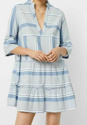 Kvinde iført en løs, knælængde kjole med horisontale og vertikale blå og hvide striber og treskvartærmer.