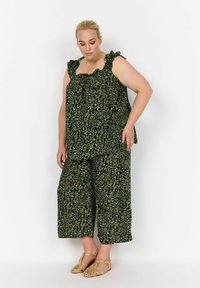 Completo leopardato verde composto da un top con volant e pantaloni a gamba larga, realizzato in tessuto leggero, abbinato a sandali intrecciati.