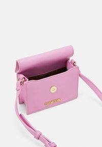 Růžová kabelka z umělé kůže na přehození s klopou, zlatými kovovými doplňky a embosovaným logem značky na přední straně. Uvnitř má vzorovanou podšívku.