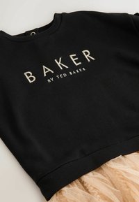 Mustat hupparit, joissa on ribbireunat kaula-aukossa ja helmassa, sisältävät kirjailun "BAKER" ja "by TED BAKER" vaaleissa väreissä. Teksturoitu kerros tülli alaosa.