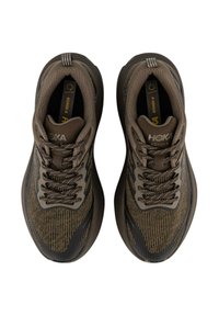 Zapatos deportivos marrones con parte superior de textil estampado, acentos oscuros y suela de goma. Presenta cordones redondos y una marca en relieve.