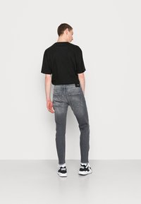T-shirt preta de manga curta combinada com jeans cinza slim-fit. Os jeans apresentam uma textura desgastada e bolsos traseiros proeminentes. Ténis preto e branco completam o visual.