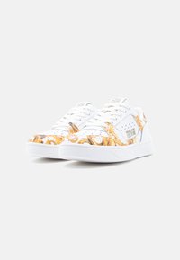 Λευκά αθλητικά παπούτσια με χρυσά και πορτοκαλί περίτεχνα σχέδια. Διαθέτουν λείο υλικό, στρογγυλεμένη μύτη και υφασμένη λαστιχένια σόλα. Κλειστές κορδόνια.