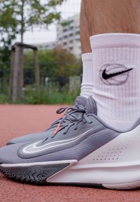 Graue Sportschuhe mit einer weißen Sohle verfügen über ein strukturiertes Obermaterial, eine orangefarbene Akzent-Schnürung und Nike-Branding, kombiniert mit weißen gerippten Socken.