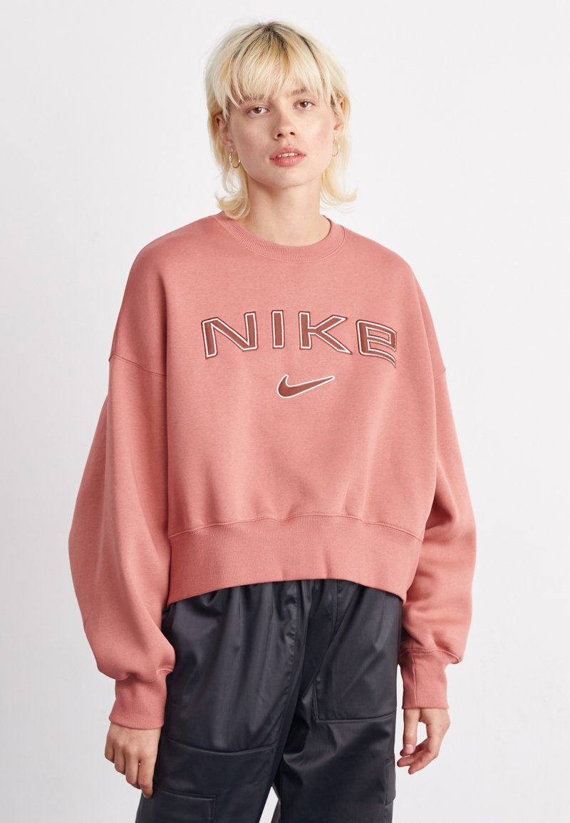 Sudadera corta rosa con el logo "NIKE" en costura contrastante. Cuenta con hombros caídos, puños acanalados y una textura suave y lisa.