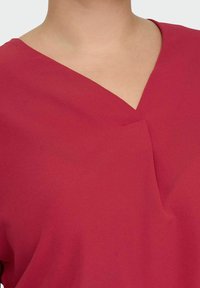 Burgundy topp med V-halsdesign, tillverkad av lätt och mjuk tyg med en flödande textur och minimalistiska sömnadsdetaljer.