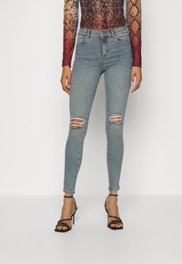 Lichtblauwe skinny jeans met versleten scheuren bij de knieën, met een hoge taille en subtiele vervaging. Gecombineerd met zwarte stringhakken.