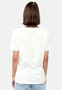 Hvid bomulds t-shirt med korte ærmer, rund halsudskæring og minimal tekstdetalje på ryggen. Blød tekstur, afslappet pasform.