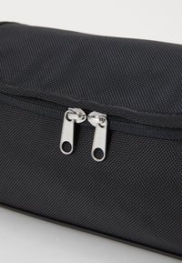 Black pouch made of textured fabric with a smooth zipper featuring two silver pulls and an open hole for attaching accessories.