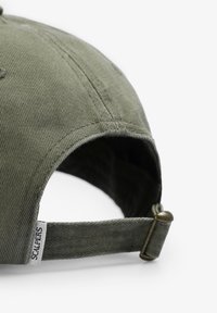 Gorra de béisbol verde oliva hecha de algodón texturizado, con una visera curvada, correa ajustable con cierre de metal y una etiqueta de marca.
