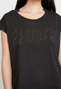 Svart kortärmad t-shirt med ordet "ALLSAINTS" i ett mönster av små metallisk stjärnor. Mjukt bomullsmaterial med avslappnad passform.