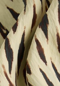 Tissu présentant un fond beige avec des bandes abstraites marron et noires, mettant en valeur une texture lisse et une tombée fluide.