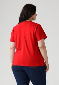 T-shirt in cotone rosso con collo rotondo e maniche corte, caratterizzata da una texture liscia e una vestibilità morbida, indossata con jeans blu scuro.