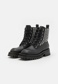 Botine negre care au un finisaj din piele netedă, talpă groasă din cauciuc și accente metalice cu ținte pe lateral, dotate cu ochiuri rotunde.