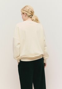 Kremowy sweter z opadającymi ramionami, ściągaczami przy mankietach i u dołu, w połączeniu z czarnymi spodniami; minimalistyczny design, miękka tekstura.