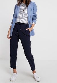 Ljust blå kordfløyelsblazer med två knappar, bärs över en randig skjorta. Navybyxor med vita sidostripor, kombineras med vita sneakers.