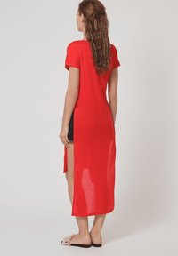 Vestido rojo de mangas cortas, hecho de una tela ligera, con aberturas laterales y una parte trasera larga, de corte holgado y diseño sencillo.