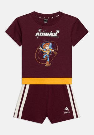 Completo Adidas per bambini color marrone scuro con rifiniture gialle, con Woody di Toy Story sulla maglietta e le strisce Adidas sui pantaloncini con il logo Pixar.