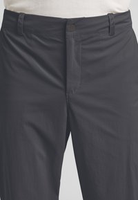 Donkergrijze broek van lichtgewicht stof. Beschikt over een ritssluiting, lussen voor een riem en een vlakke voorkant met minimale naden en een subtiele textuur.