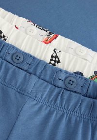 Zwei Paar Hosen: eine blau, die andere mit einem weißen Bund, der ein buntes Rennauto und karierte Muster zeigt. Beide haben Knopfdetails.