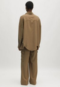 Braunes, übergroßes Hemd mit Kragen, Rückenpasse und abgesenkten Schultern, kombiniert mit passenden, weit geschnittenen Hosen mit Vorderseiten-Taschen.