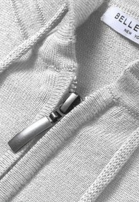 Felpa con zip grigia chiara e texture a coste, con cerniera argentata e linguetta. L'etichetta recita "BELLE NEW YORK."