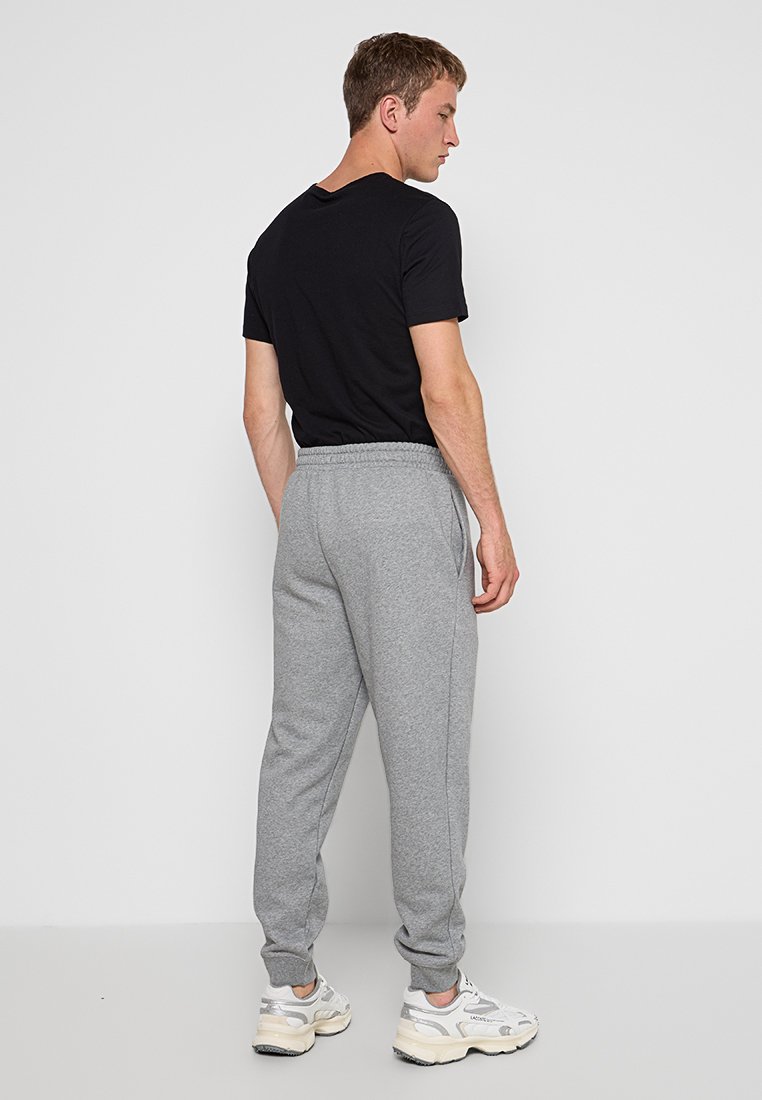 Pantalons de survêtement gris avec taille élastique, poches latérales et jambes fuselées, portés avec un t-shirt noir et des chaussures de sport blanches.