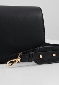 Borsa a mano in pelle nera di forma rettangolare, con chiusura in metallo dorato e tracolla in pelle. Texture liscia con dettagli di design minimalisti.