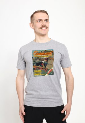 Šedé bavlněné tričko s barevnou retro grafikou skateboardového magazínu na přední straně, se textem a obrázkem skateboardisty.