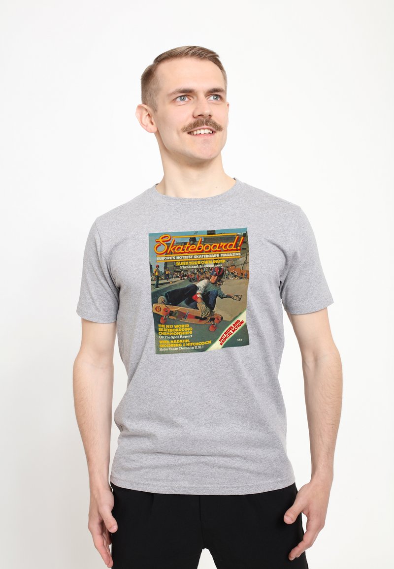 Šedé bavlněné tričko s barevnou retro grafikou skateboardového magazínu na přední straně, se textem a obrázkem skateboardisty.