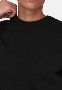 Sweatshirt en coton noir avec un col rond côtelé. Le tissu semble doux et lisse, sans motifs ni designs visibles.