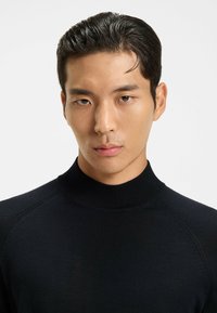 Maglione nero a collo alto, tessuto lavorato a maglia con texture liscia, caratterizzato da un design aderente e colletto e polsini a coste.