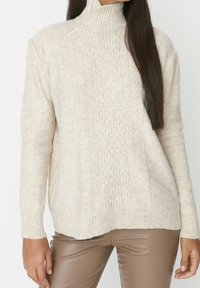 Pullover in Cremefarbe mit hohem Kragen, strukturiertem Zopfmuster, langen Ärmeln, gerippten Bündchen und einem leicht übergroßen Sitz.