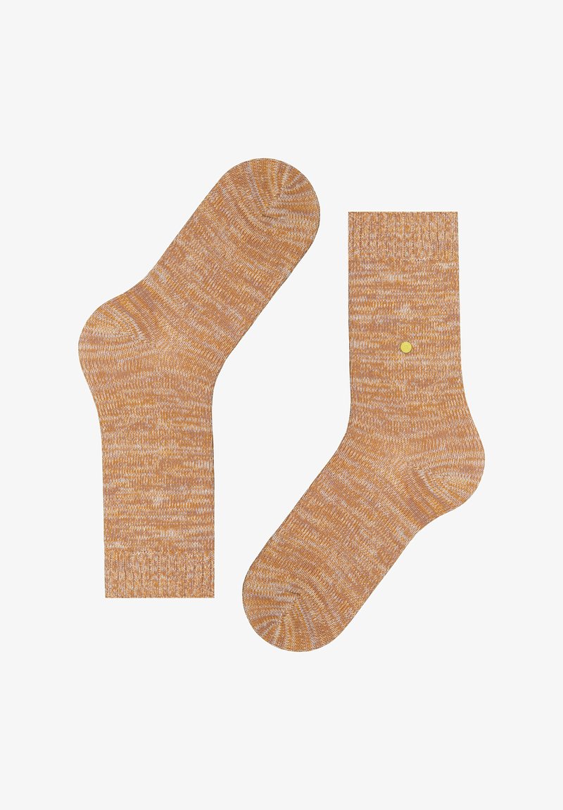 Une paire de chaussettes en tricot marbré jaune moutarde et blanc, l'une posée à plat et l'autre montrant l'avant avec un petit détail en point jaune.