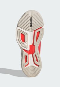Suela de zapatilla deportiva de goma, con un diseño en rojo y beige, texturizada para ofrecer tracción, con un logotipo prominente y una superficie que no deja marcas.