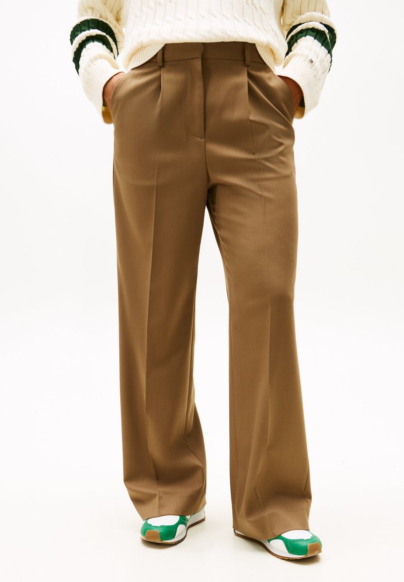 Spodnie o szerokich nogawkach z lekkiego brązowego materiału o gładkiej fakturze i przednich zakładkach. Dopasowane do wielokolorowych butów sportowych.