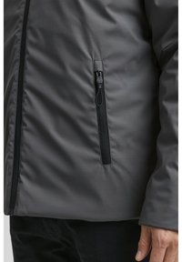 Grå isolerad jacka med slät textur, med en ficka med dragkedja på vänster sida och svart dragkedja. Enkel, funktionell design.