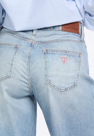 Jeans in denim azzurro chiaro con un design a cinque tasche, che presentano un distintivo logo a triangolo rosso sulla tasca posteriore e una patch in pelle sulla vita.