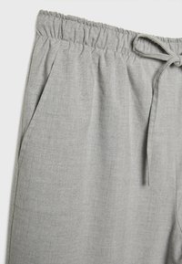 Jasnoszare spodnie z elastycznym paskiem w talii, boczną kieszenią i sznurkiem na górze na jednolitym tle.