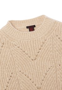 Beige gestrickter Pullover mit einem gerippten Kragen, einem strukturierten Rautenmuster und einem Etikett mit "Made in Italy" in Rot und Schwarz.
