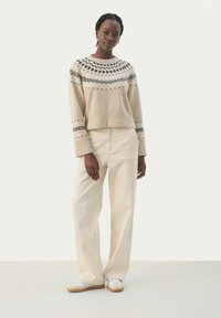 Pull en tricot beige avec un motif noir, associé à un pantalon large crème et des baskets blanches avec des accents beige et gris.