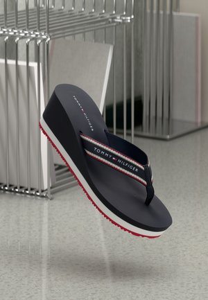 Marineblå Tommy Hilfiger kile-sandaler med rød, hvid og sort striped rem og rød tekstureret sål på grå gulvbaggrund.