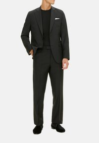 Completo nero su misura con giacca monopetto, pantaloni abbinati e una camicia nera semplice. Include un fazzoletto bianco da taschino. Texture liscia.