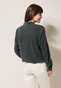 Grünes, strukturiertes Langarmhemd mit Kragen, Rückansicht; getragen mit hellen, figurbetonten Hosen; lässiges Design.