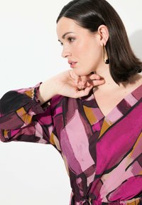 Langärmlige Bluse mit einem lebendigen, abstrakten Muster aus Pink, Lila und Gelb. Sie verfügt über einen V-Ausschnitt und geraffte Ärmelbündchen.