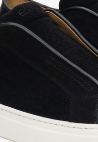 Czarne zamszowe buty typu slip-on z skórzanymi akcentami, z białą gumową podeszwą i tonowym przeszyciem. Minimalistyczny design i gładka faktura.