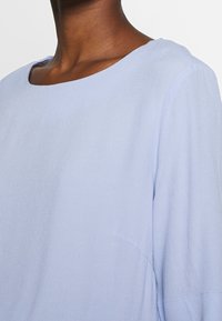 Maglia a maniche lunghe di colore azzurro chiaro con scollatura tonda, in tessuto morbido e testurizzato, con cuciture sottili e vestibilità rilassata.