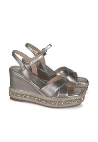Sandali wedge metallici argento con cinturini incrociati, chiusura alla caviglia e base decorata con perline e dettagli ornamentali.