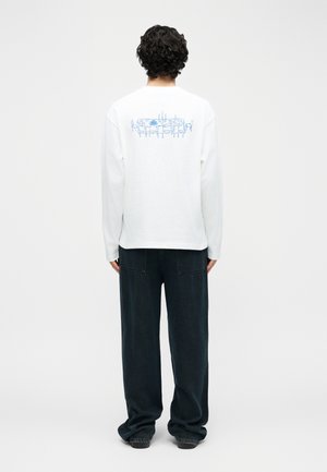 Άτομο με σγουρά μαλλιά στέκεται με την πλάτη, φοράει λευκό μακρυμάνικο πουκάμισο με μπλε γραμμικό σχέδιο τραπεζιού φαγητού στην πλάτη.