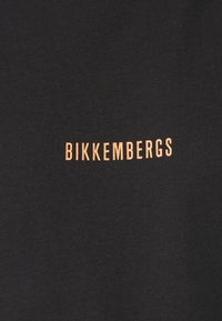 Camiseta negra de tela suave con "BIKKEMBERGS" impreso en letras negritas de color cobre, centrado en la parte inferior.